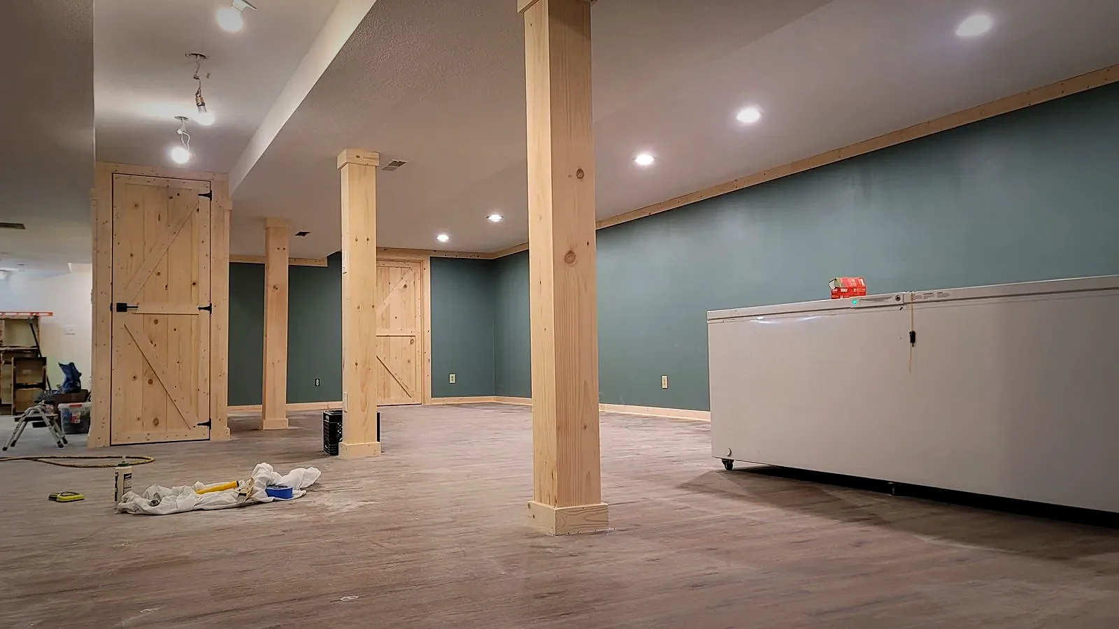 Finished basement room with box-beam columns, crown molding, and custom barn doors